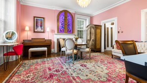 A room with a piano, a dining table with chairs, a large rug, a chandelier, and a stained glass window. - Stay in Historic Bucks County Farmhouse
Sleeps 18 -13 beds, 5 baths, 2 kitchens  (Bensalem)
