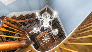 A grand staircase with a chandelier, wooden balustrades, and a patterned carpet. - Stay in Historic Bucks County Farmhouse
Sleeps 18 -13 beds, 5 baths, 2 kitchens  (Bensalem)