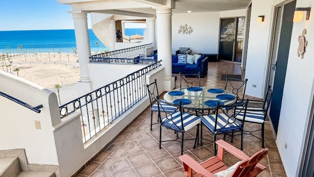 Un balcon avec vue sur la plage, une table ronde en verre avec des chaises et un canapé.