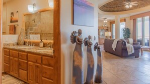 Une salle de bain avec un grand miroir, des meubles en bois et un lavabo. On y trouve également des éléments décoratifs sur les murs et un ventilateur de plafond.