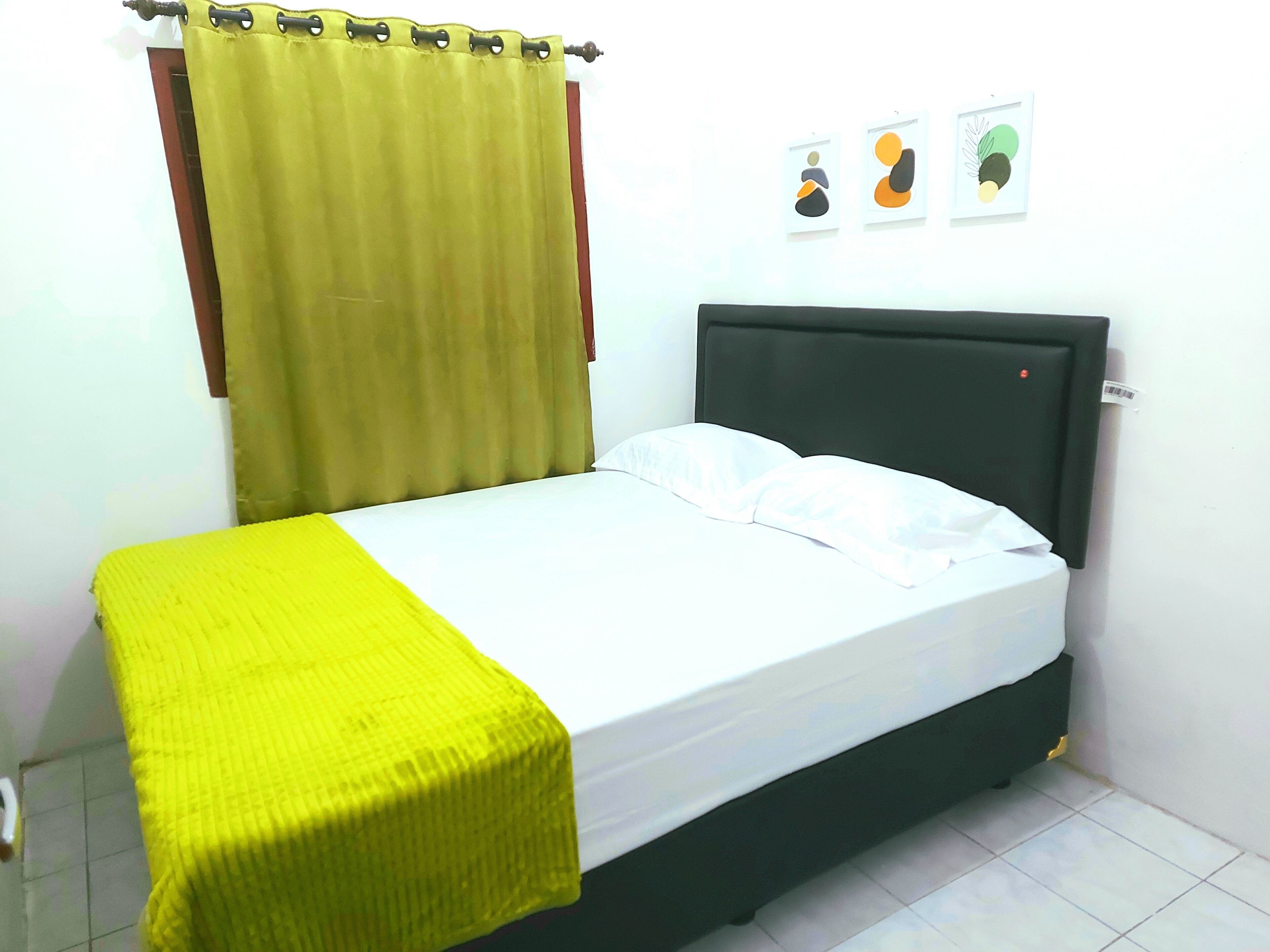 A bed with a black headboard, a yellow bedspread, and a green curtain. There are three framed pictures on the wall.