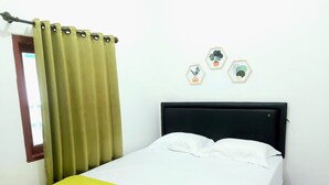 Ein Bett mit schwarzem Kopfteil, einer gelben Bettdecke und einem grünen Vorhang. Es sind drei sechseckige Wanddekorationen zu sehen.
