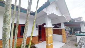 Ein zweistöckiges Haus mit weißer Fassade, roter Tür und überdachter Veranda.