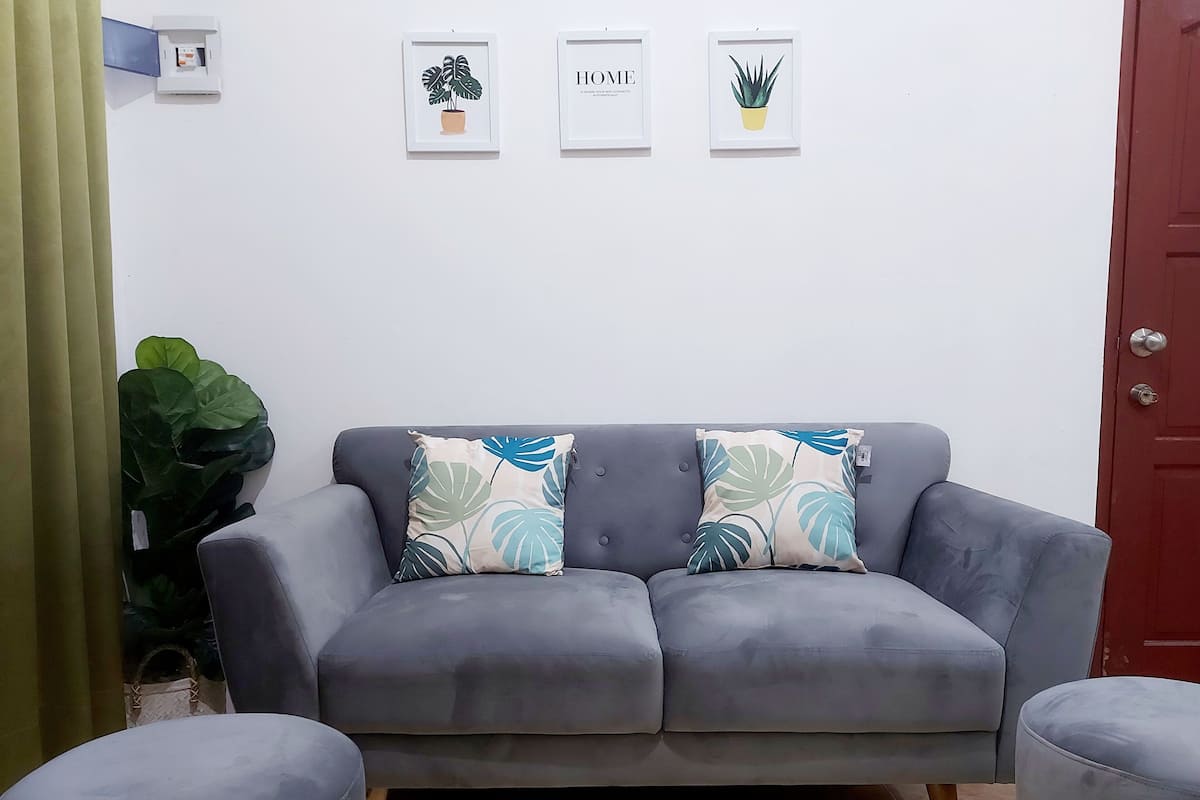 A grey sofa with two decorative pillows, a small table, and a potted plant.