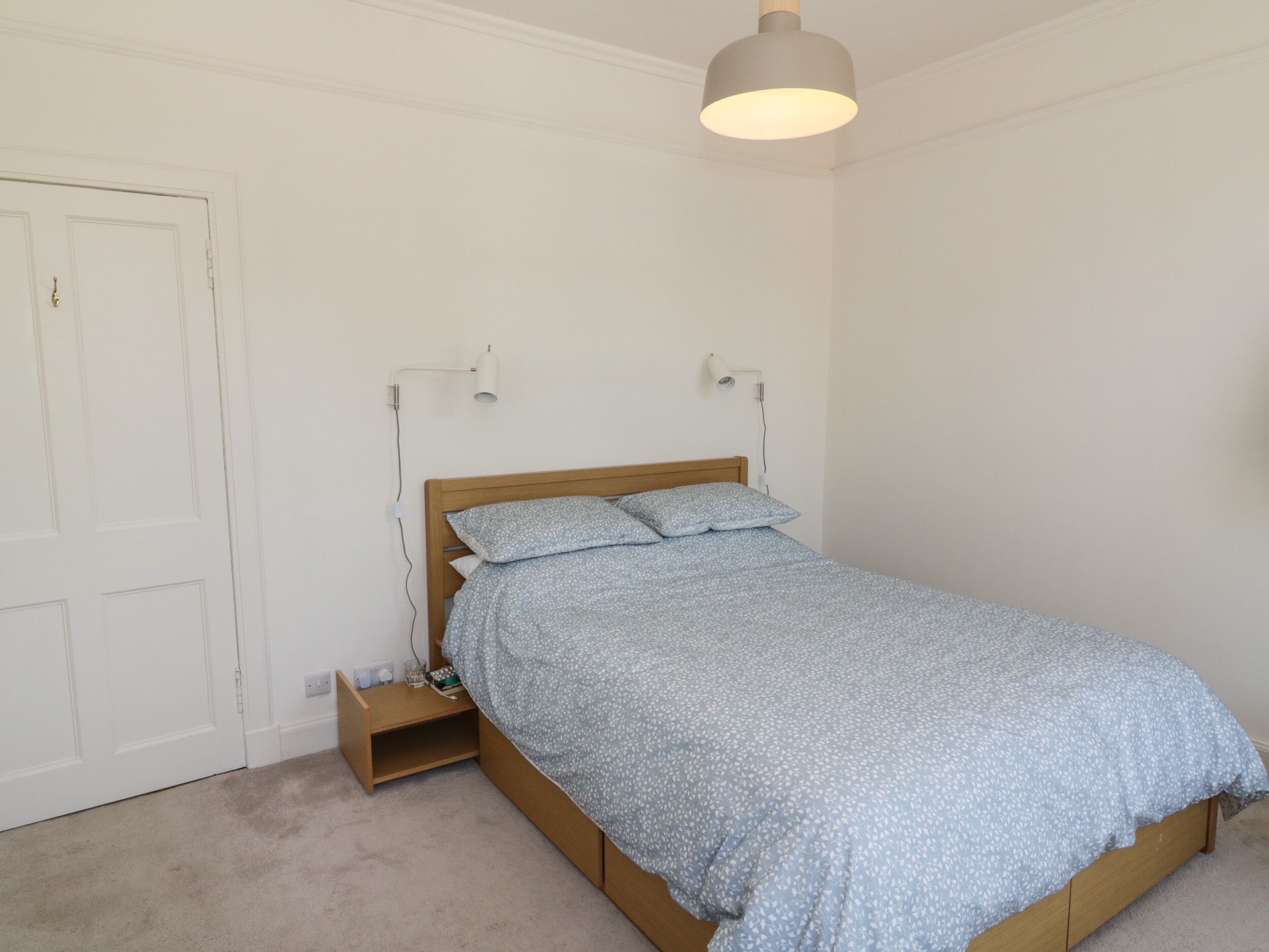 A bedroom with a wooden bed, a nightstand, a lamp, and a door.