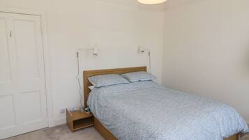 A bedroom with a wooden bed, a nightstand, a lamp, and a door.