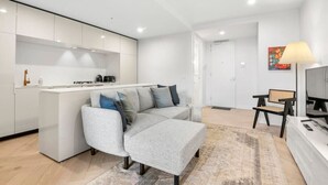 A modern apartment with a grey sofa, a small kitchen, a dining area, and a TV. - Artistic Getaway by Artist Abodes (Fitzroy)