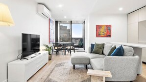 A modern living room with a flat-screen TV, a grey sofa, a dining table with chairs, and a balcony with a view. - Artistic Getaway by Artist Abodes (Fitzroy)