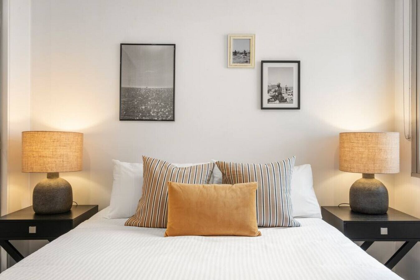 Quarto de hotel com uma cama, duas mesas de cabeceira, duas luminárias e duas fotos emolduradas na parede.