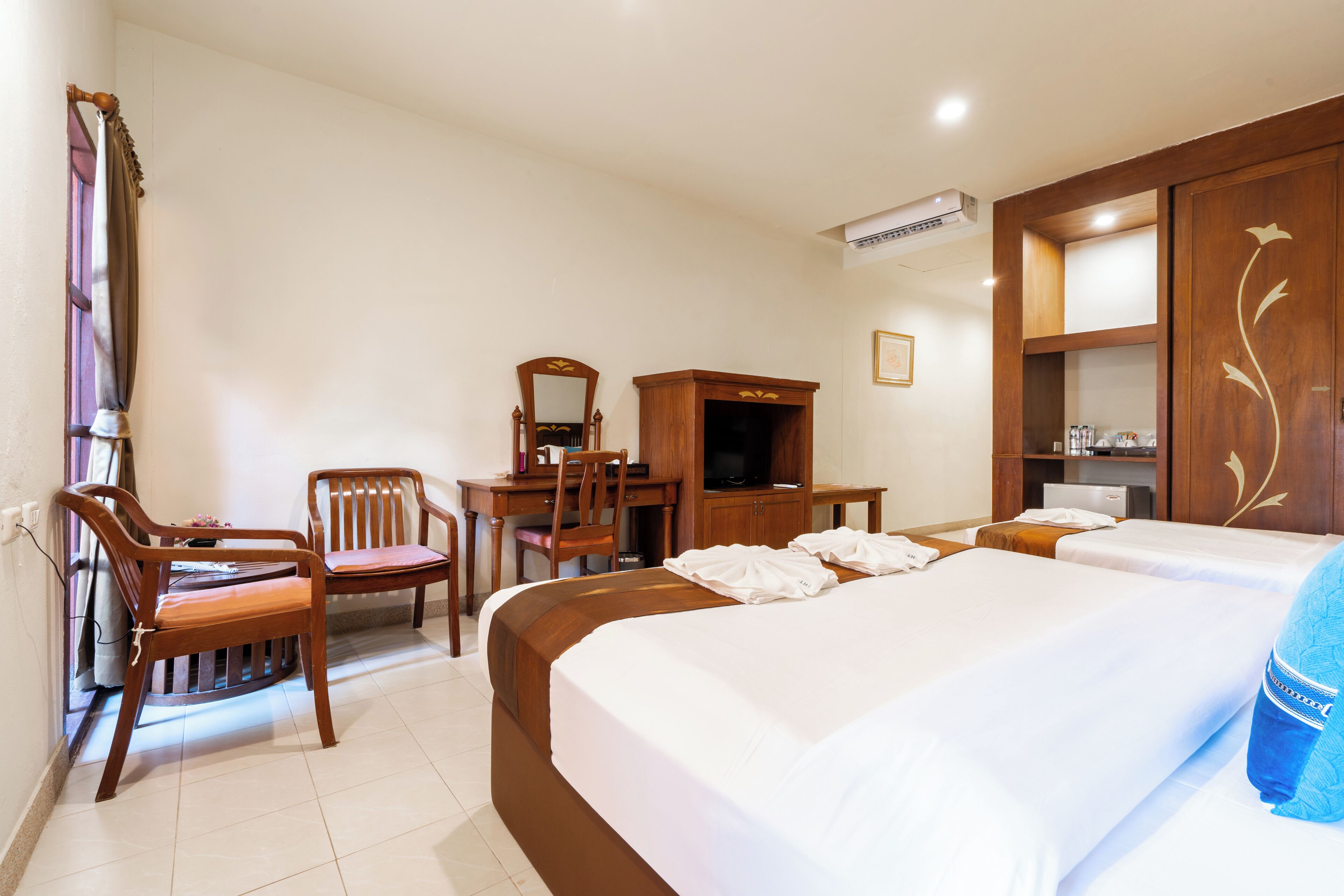 A hotel room with two beds, a desk with a chair, a television, and a wardrobe.