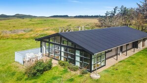 A modern house with large glass windows, a flat roof, and a patio area with outdoor furniture.