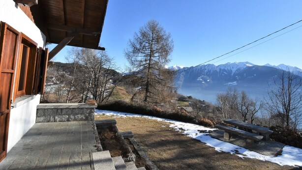 A wooden building with stone steps leading to a bench overlooking a snowy landscape and mountains. - Chalet Elda by Interhome (Mello)