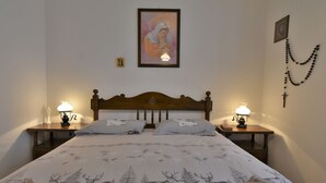 A neatly made bed with a deer print bedspread, two bedside lamps, a framed picture above the bed, and a rosary on the wall. - Chalet Elda by Interhome (Mello)