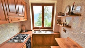 A kitchen with wooden cabinets, a gas stove, a sink, and a window with a view of trees. - Chalet Elda by Interhome (Mello)