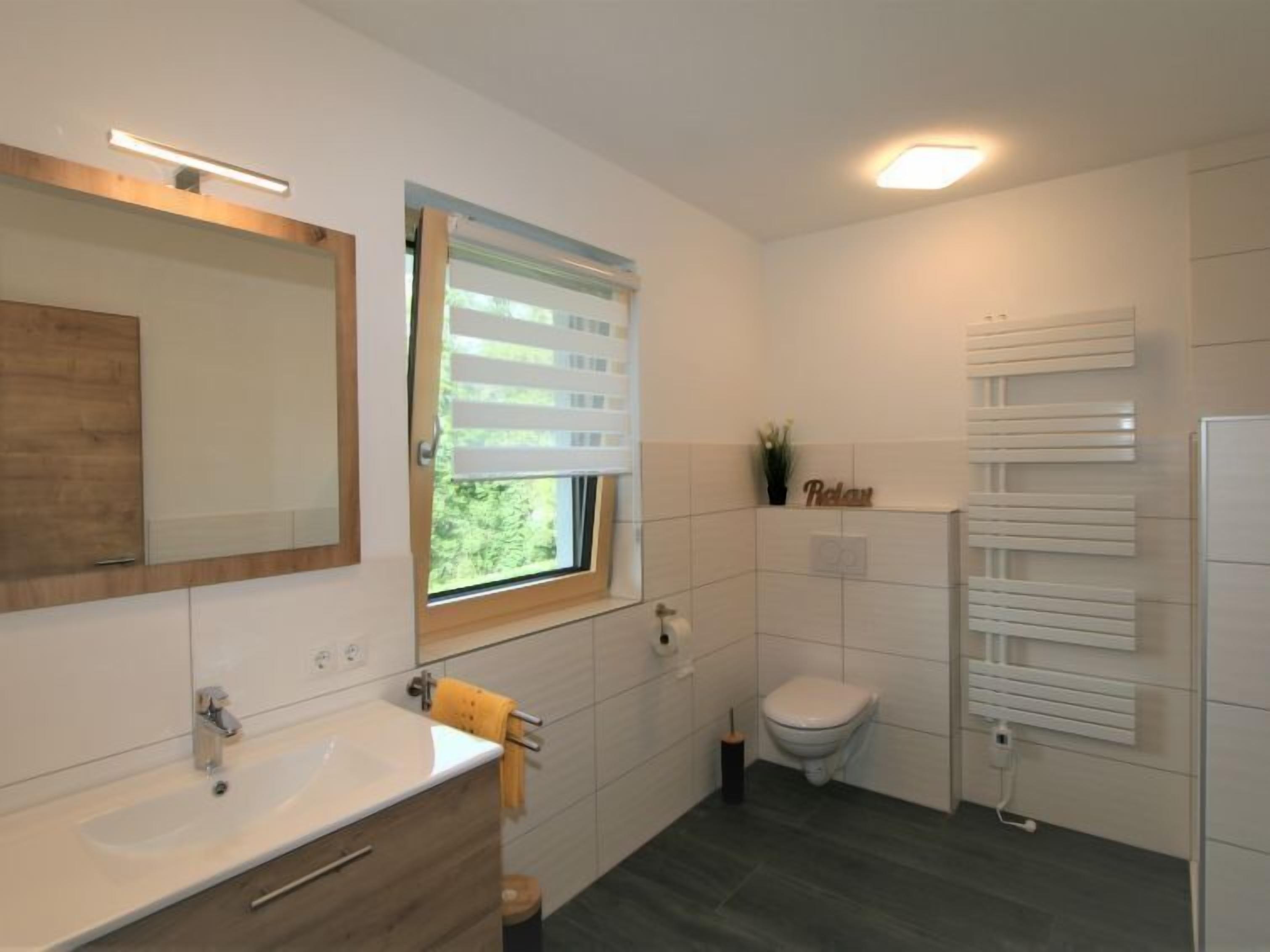 A modern bathroom with a wooden vanity, a toilet, and a towel rack.