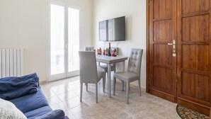 A room with a sofa, a dining table with chairs, a TV mounted on the wall, and a wooden door. - Apartment Maria by Interhome (Sanremo)