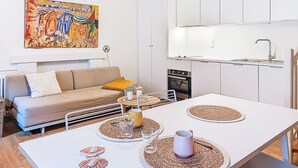 Cozinha moderna com armários brancos, forno embutido e área de refeições com mesa branca e jogos americanos.
