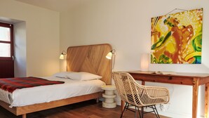 Quarto com cama de madeira, uma escrivaninha, uma cadeira e um quadro na parede.