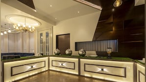 A reception area with a modern design, featuring a reception desk, a chandelier, and a large mirror. - Treebo Prasha (Nashik)