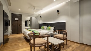 A modern hotel room with a large bed, two wooden chairs, a small table, a ceiling fan, and a wall-mounted TV. - Treebo Prasha (Nashik)