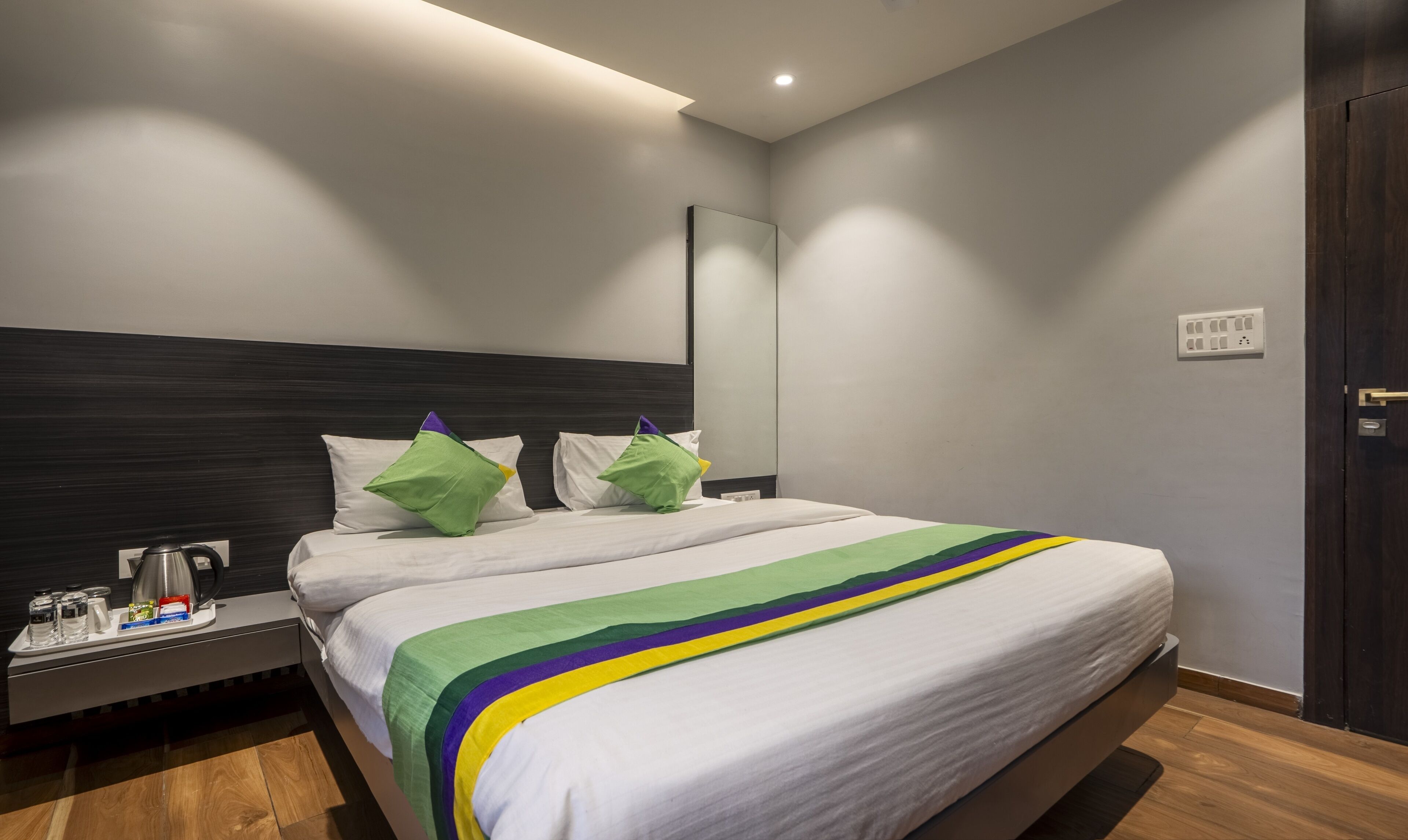 A modern hotel room with a large bed, a bedside table with a kettle, and a nightstand.