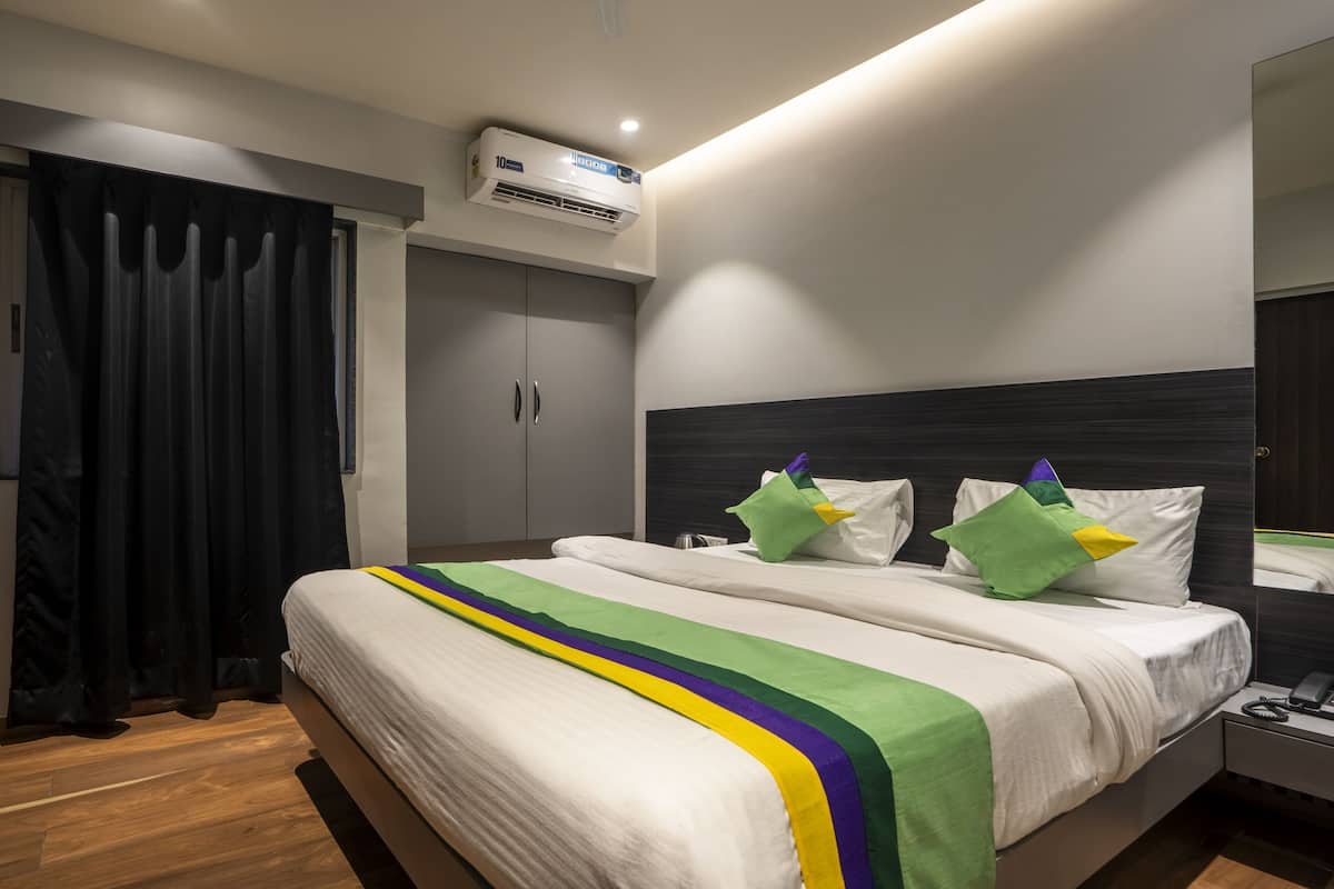 A hotel room with a bed, a wardrobe, a mirror, and an air conditioning unit.