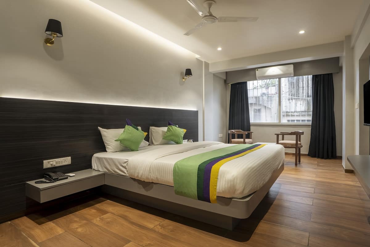 A modern hotel room with a large bed, bedside table with a phone, a flat-screen TV mounted on the wall, and a window with curtains.
