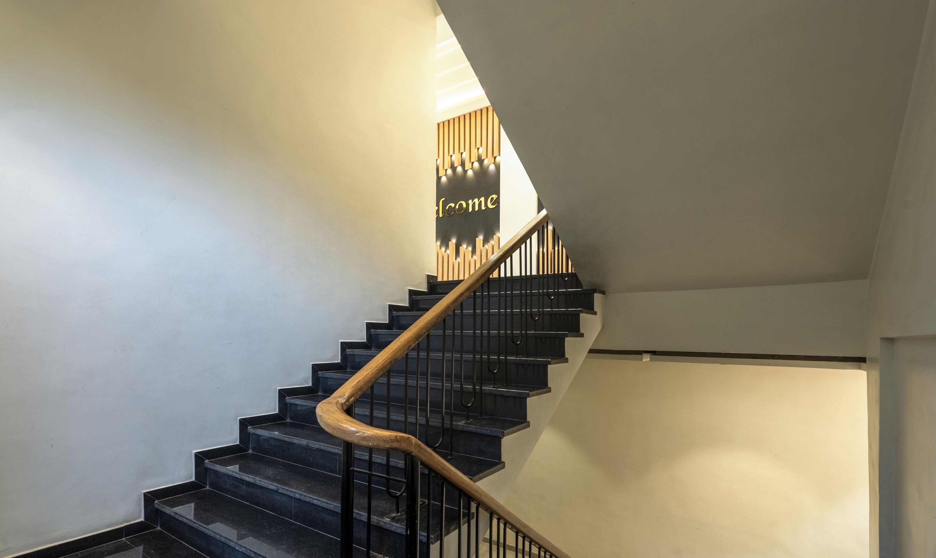 A staircase with black steps and a wooden handrail, leading to a landing with a 'Welcome' sign.