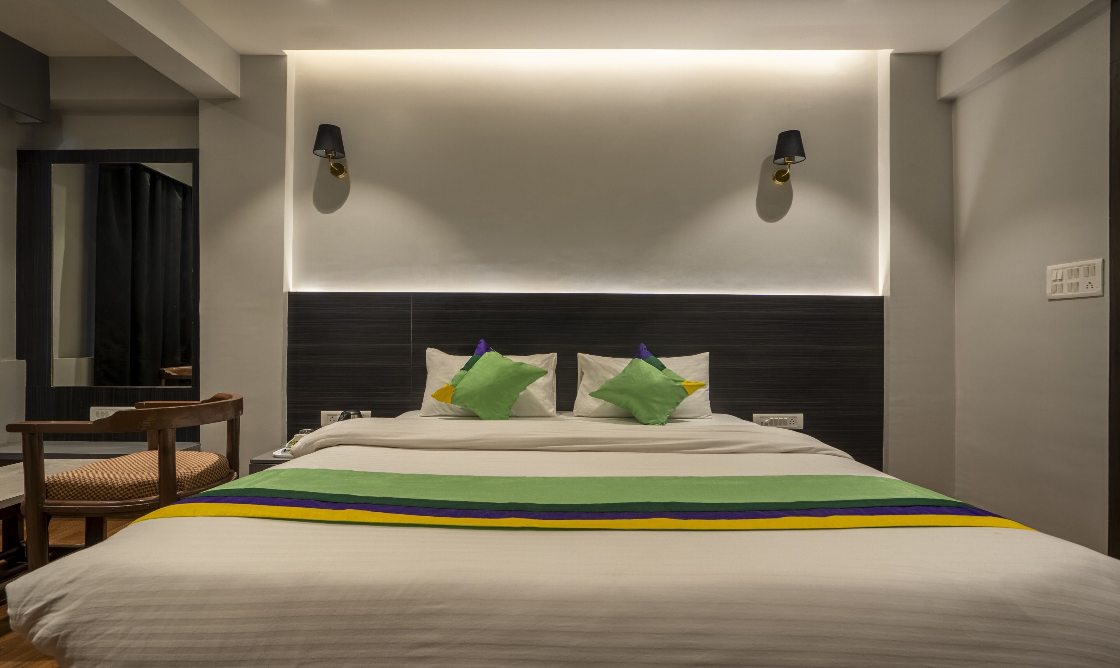 A hotel room with a bed, a nightstand, a chair, and a mirror.