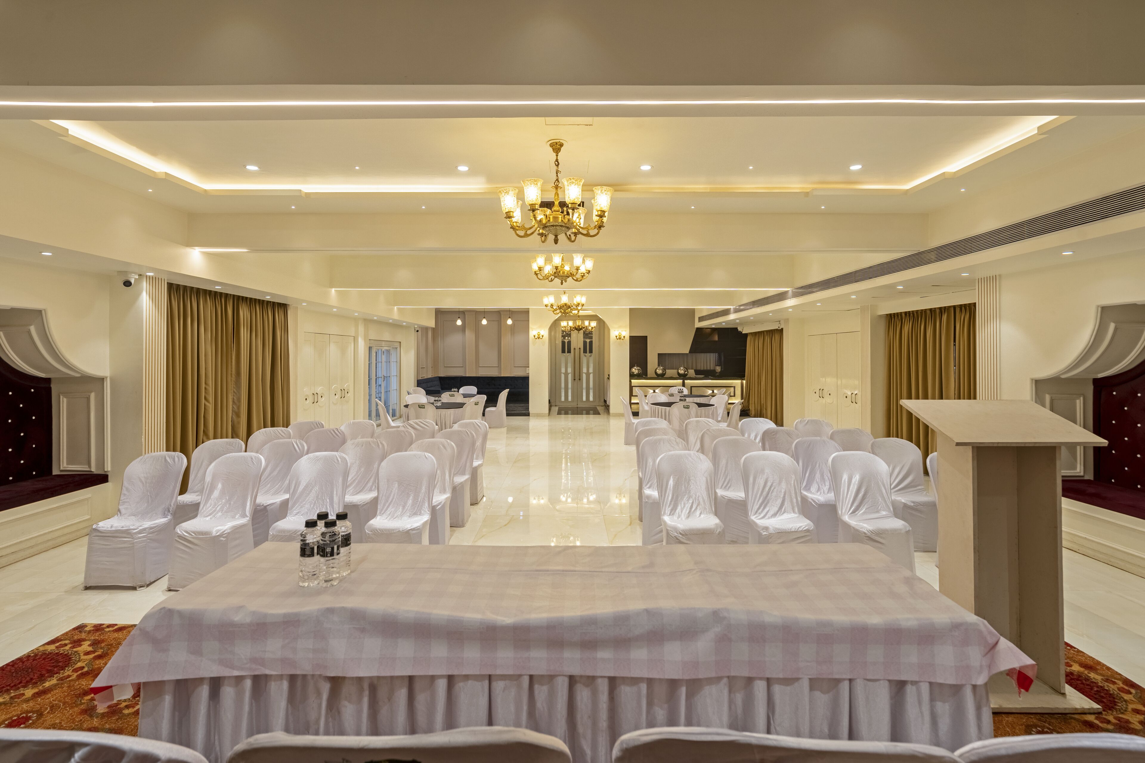 A spacious banquet hall with a long table, white chairs, and a chandelier.