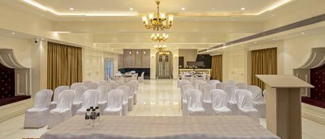 Un amplio salón de banquetes con una larga mesa, sillas blancas y una araña.