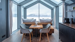 A modern interior with a large skylight, a wooden table, two chairs, and a bench with cushions. - AERA - Aurora Glass Cabins (Tromsø)