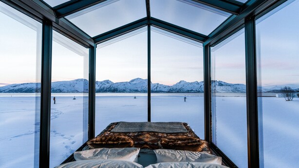 A room with a glass ceiling, a bed with white and brown bedding, and a snowy landscape view. - AERA - Aurora Glass Cabins (Tromsø)
