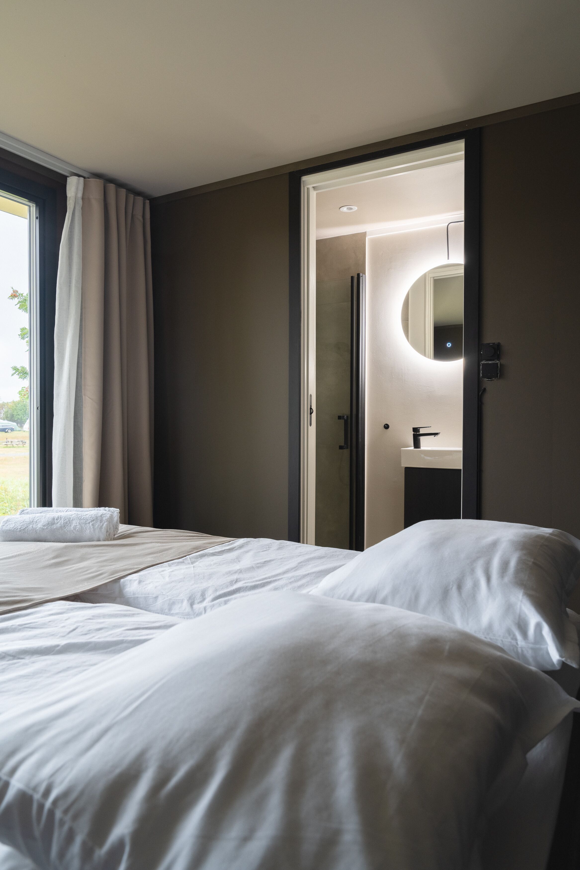 A hotel room with a bed, a bathroom with a mirror and sink, and a view of the outdoors.