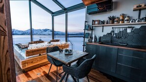 A modern interior with a large window, wooden furniture, and a kitchen area with shelves and jars. - AERA - Aurora Glass Cabins (Tromsø)