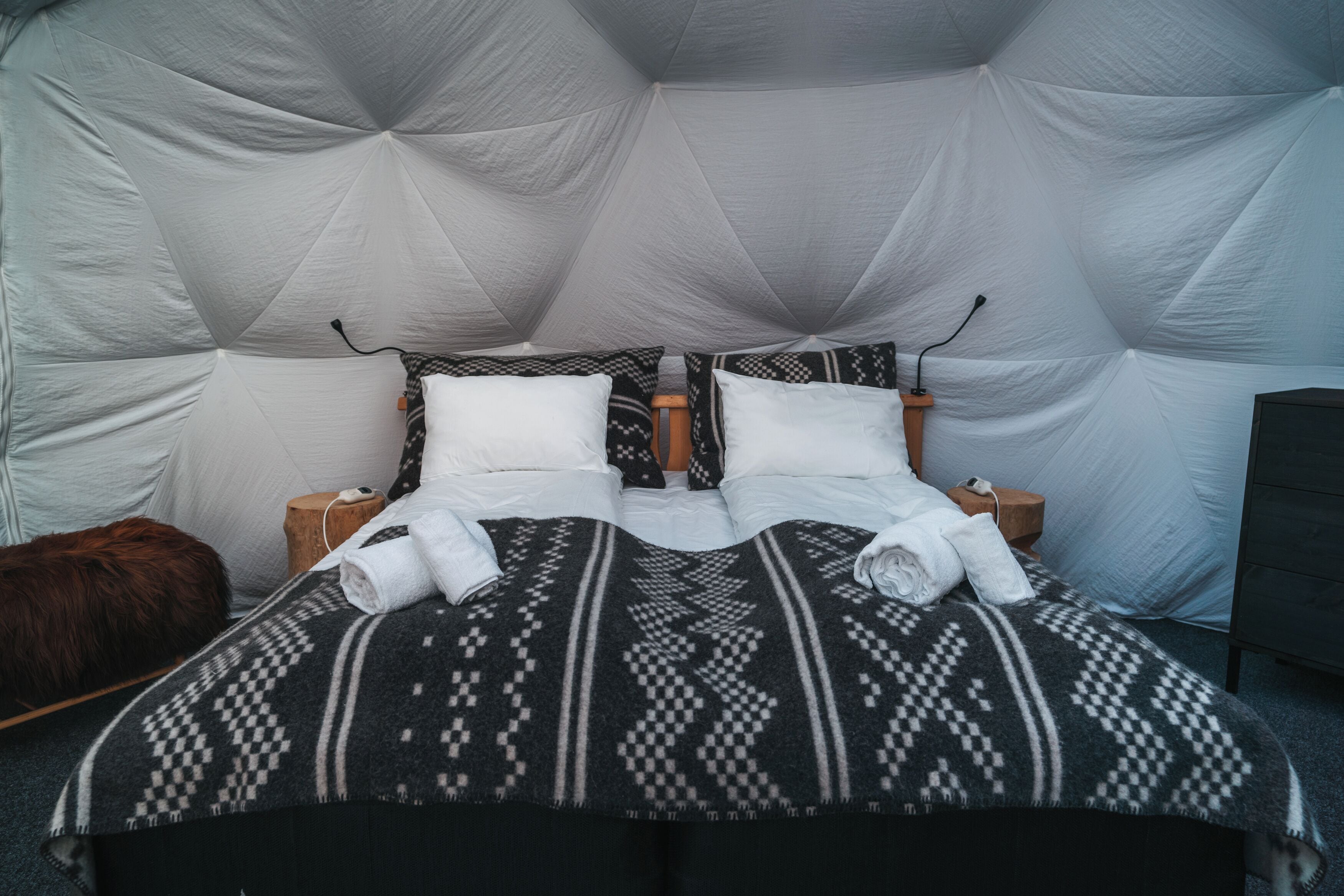 A bed with a geometric patterned blanket, two pillows, and a fluffy brown pillow.