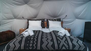 A bed with a geometric patterned blanket, two pillows, and a fluffy brown pillow.