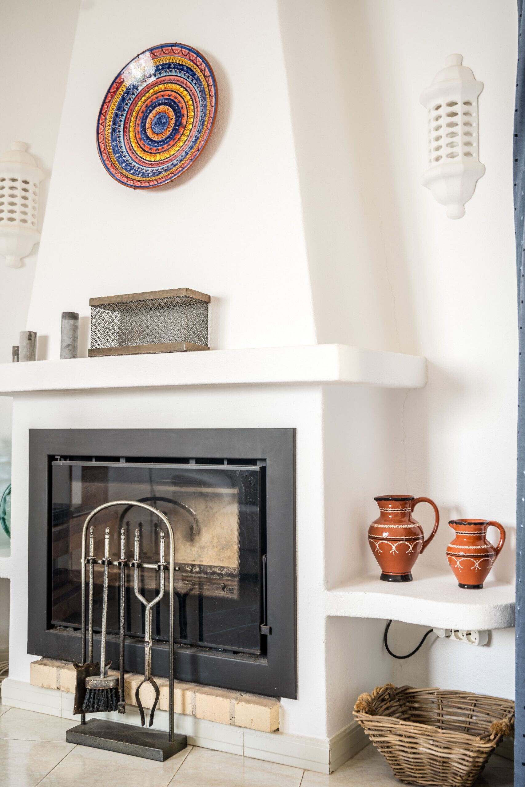 A fireplace with a metal grate, a decorative plate above it, and two pottery pieces on a shelf below.