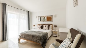 Ein Schlafzimmer mit einem Bett, Nachttischen, einem Schreibtisch, einem Stuhl, einem Spiegel und einem Fenster mit Vorhängen.