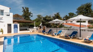 Ein Swimmingpool mit blauen Fliesen, umgeben von Liegestühlen und Sonnenschirmen.