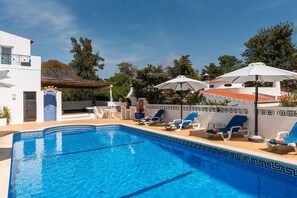 A swimming pool with blue tiles, surrounded by lounge chairs and umbrellas.