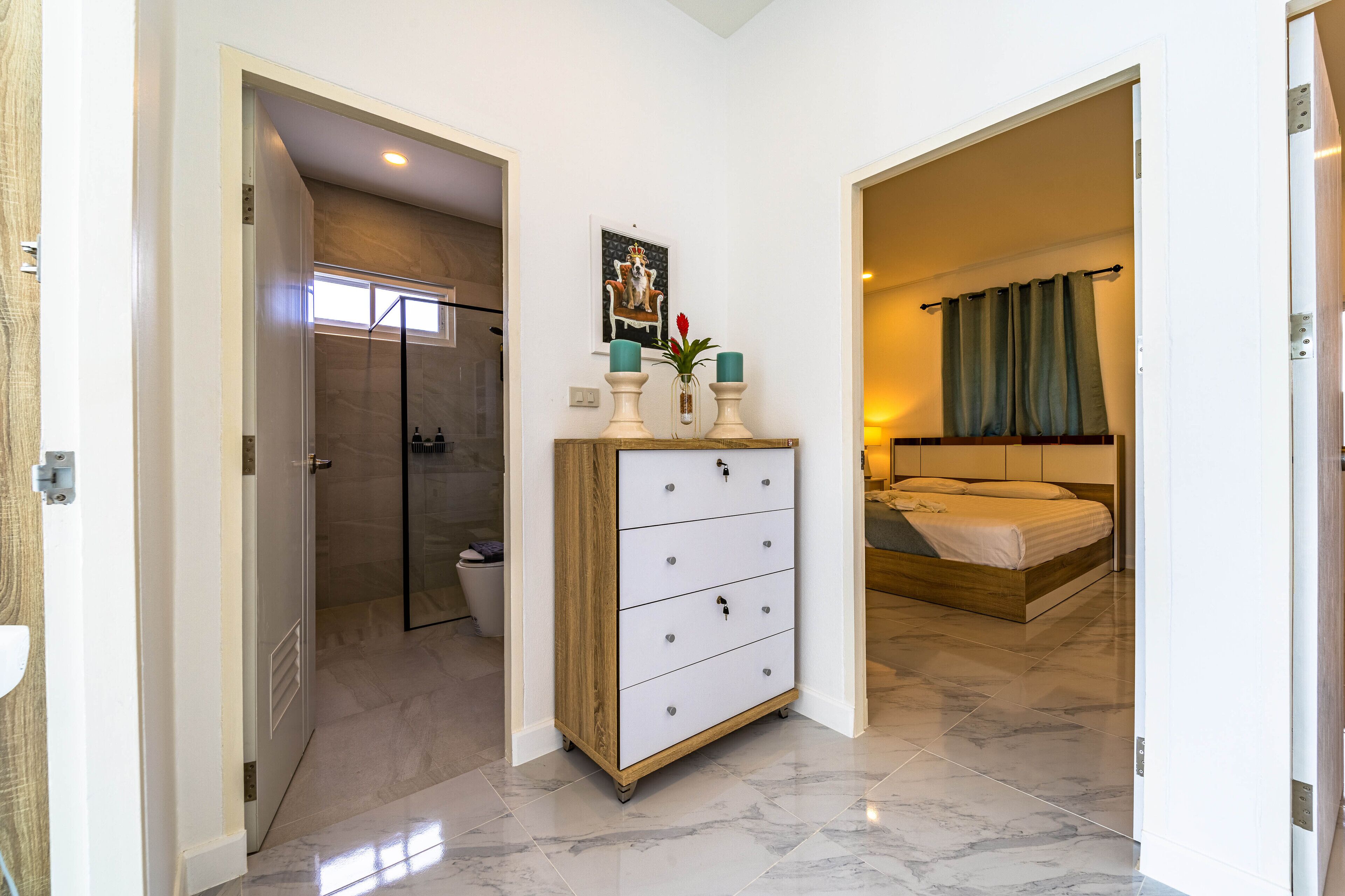 A hotel room with a marble floor, a wooden dresser with drawers, a bed with a wooden headboard, and a bathroom with a shower and toilet.