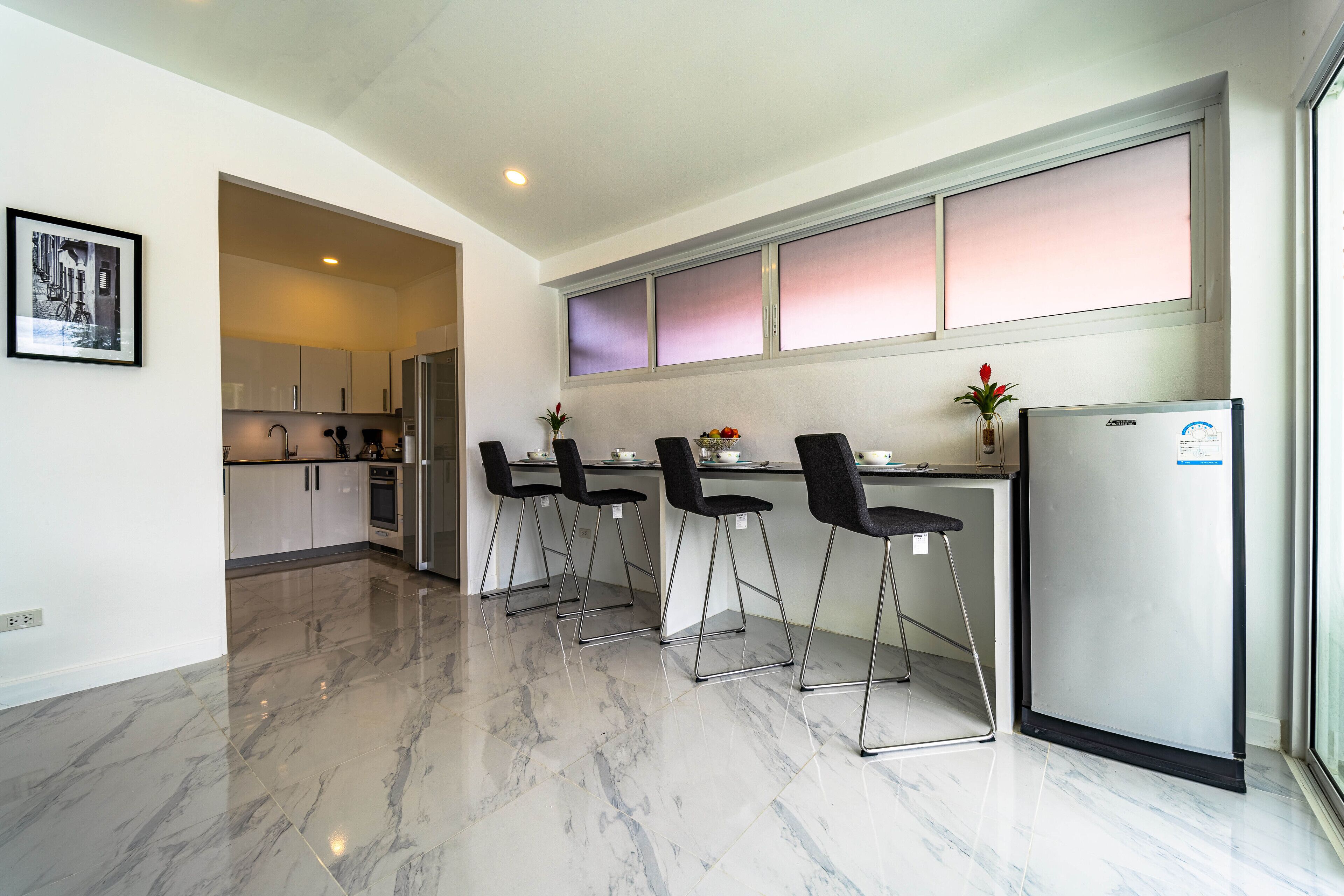 A modern kitchen with a marble floor, a refrigerator, and a dining area with chairs.