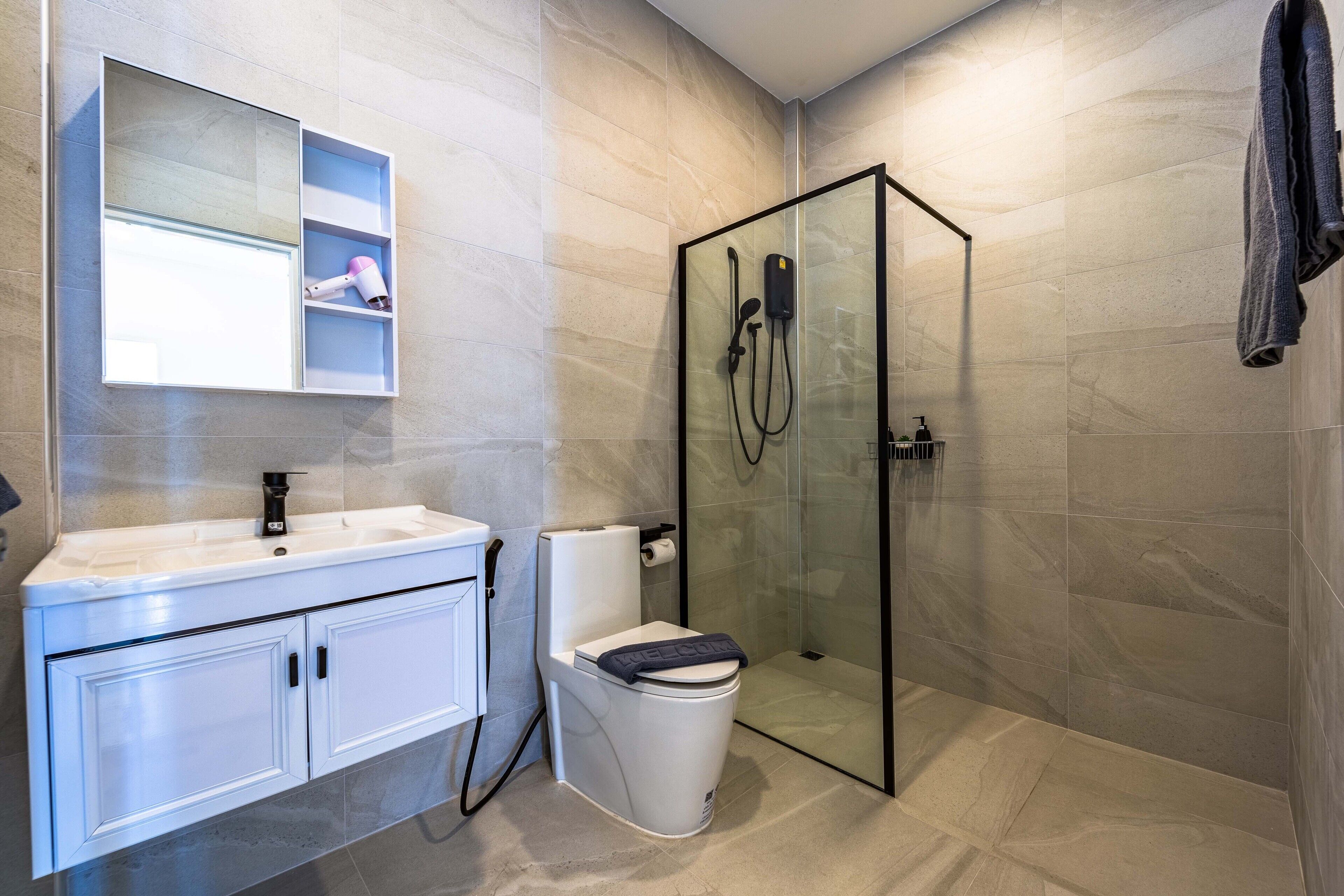 Ein modernes Badezimmer mit einer gläsernen Dusche, einem weißen Waschbecken mit Spiegel darüber und einer Toilette mit blauem Deckel.