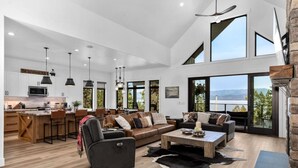 A spacious living area with a large sofa, a coffee table, and a fireplace. There is a kitchen area with modern appliances and a dining space. - Luxury Lakeside Retreat w/ Panoramic Flathead View (Lakeside)