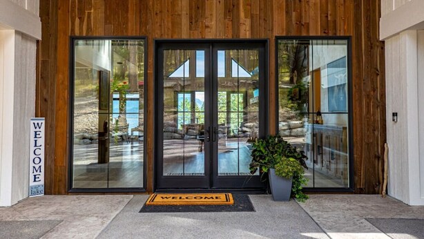 A wooden exterior with large glass doors, a welcome mat, and a sign. - Luxury Lakeside Retreat w/ Panoramic Flathead View (Lakeside)