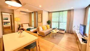 Una habitación de hotel moderna con zona de comedor, sofá, televisión y un amplio ventanal con cortinas.