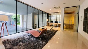 Un moderno vestíbulo de hotel con un amplio ventanal, una zona de estar con alfombra y una escalera que lleva a un nivel superior.