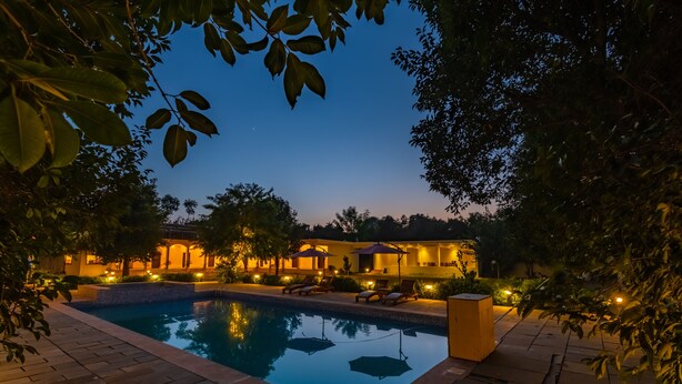A swimming pool surrounded by a patio area with lounge chairs and umbrellas. - Prakriti The Nature Resort Pushkar (Pushkar)