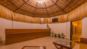 A reception area with a thatched roof, wooden reception desk, and a decorative table with a patterned tabletop. - Prakriti The Nature Resort Pushkar (Pushkar)
